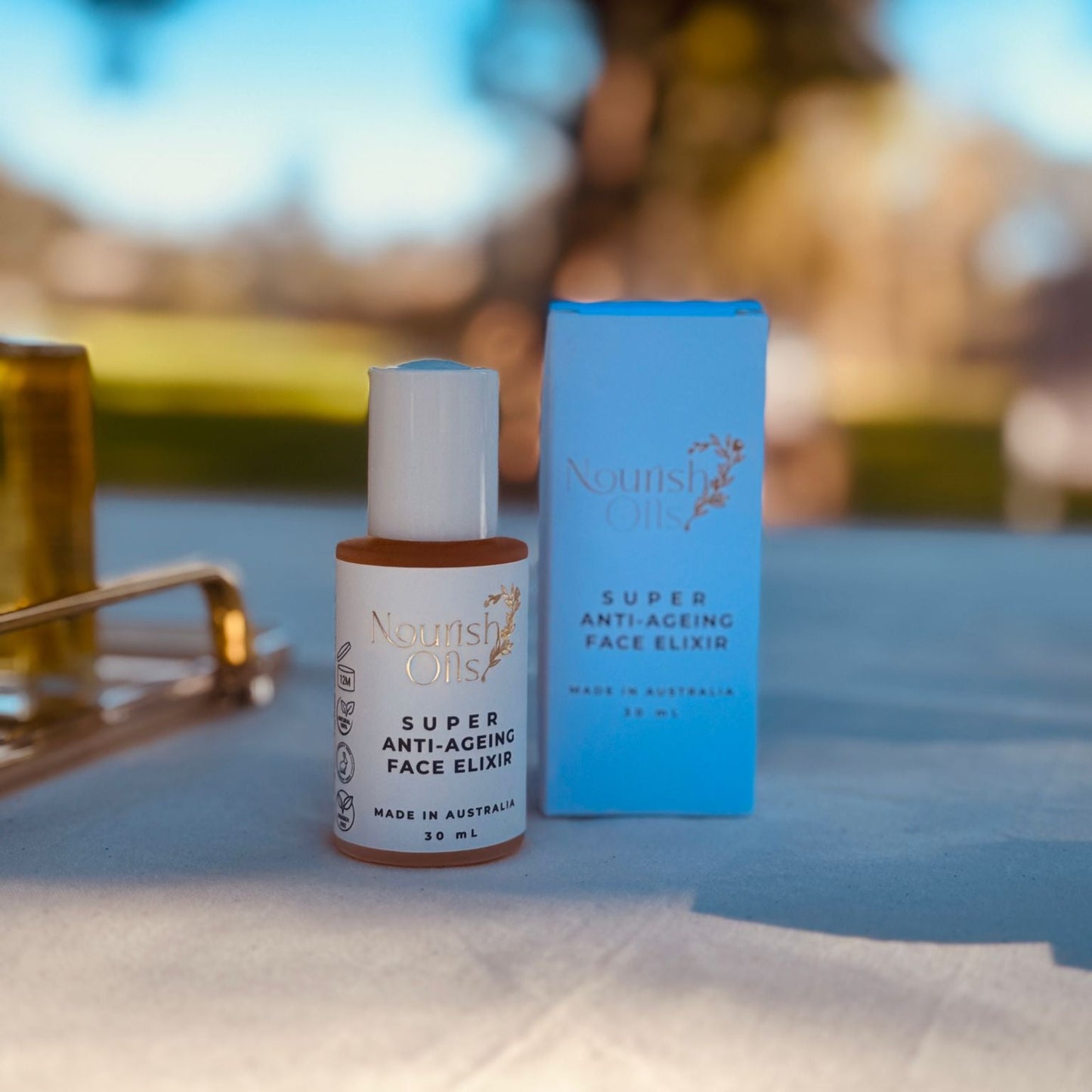 Super Anti-Ageing Face Elixir bottle and packaging on a blurred outdoor background
