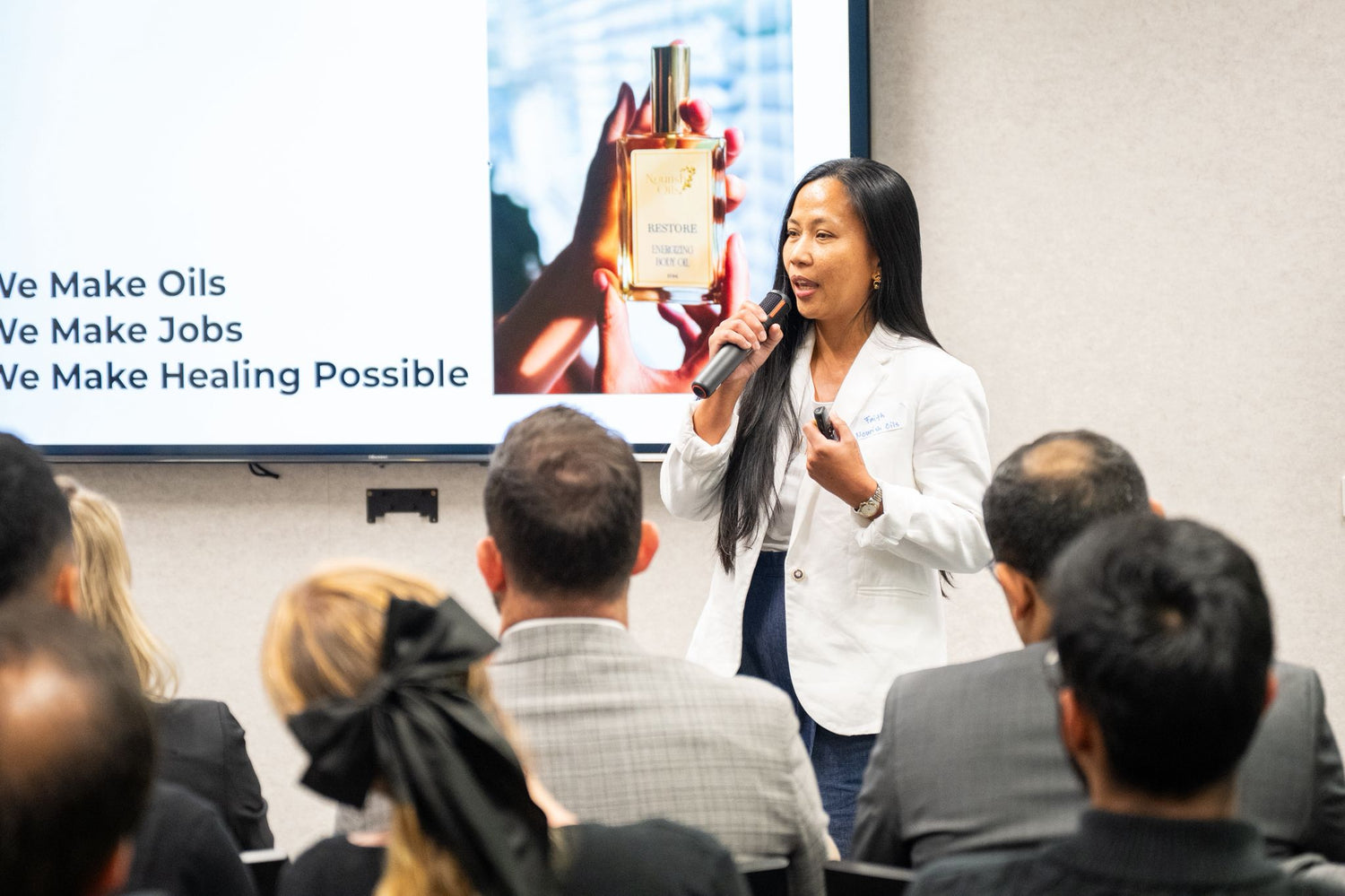 Woman giving a presentation in front of an audience with a screen displaying a product image and text.