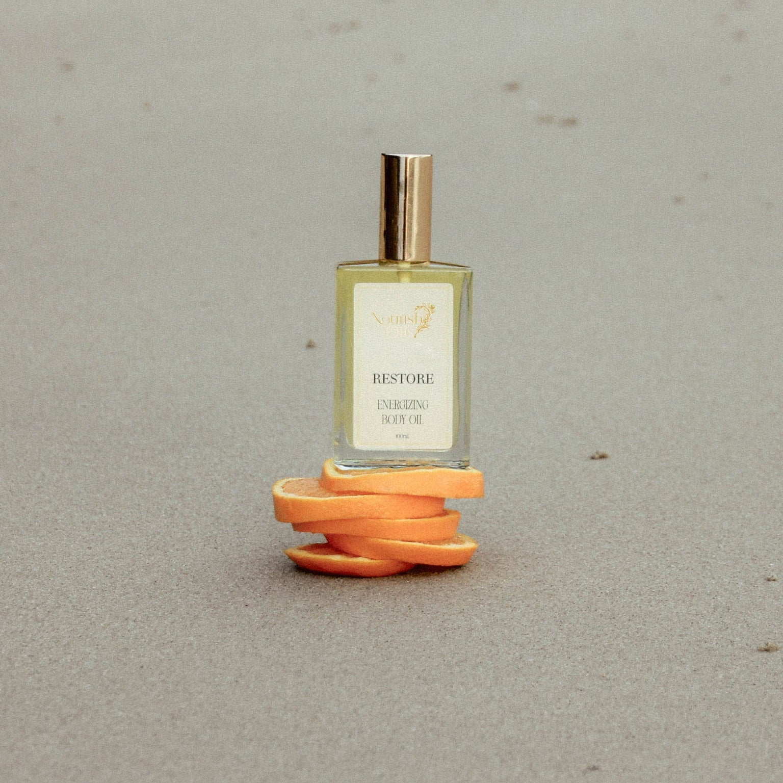 A small rectangular perfume bottle with a gold cap stands on a spiral of orange peel slices against a neutral gray background. The bottle label reads 'RESTORE' and 'FRESH BREEZE'.