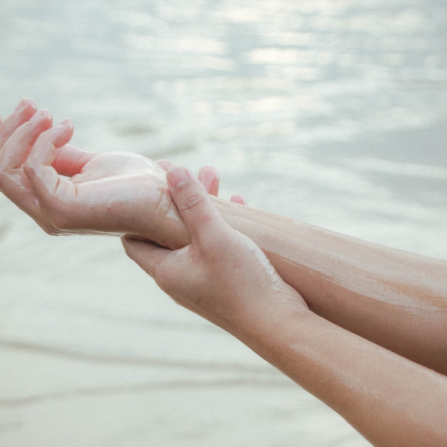 Close-up of a person's hands and forearm receiving or applying a white cream or lotion, with a softly blurred beach or water background.