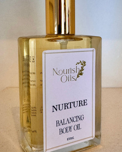 Bottle of Nourish Oils Nurture Balancing Body Oil on a beige surface with a blurred background