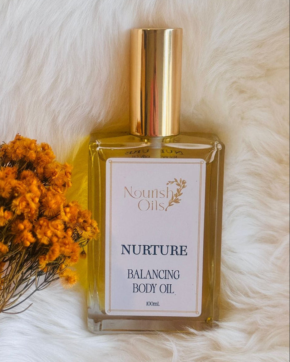 Body oil bottle labeled 'Nurture' with dried flowers on a white fur background