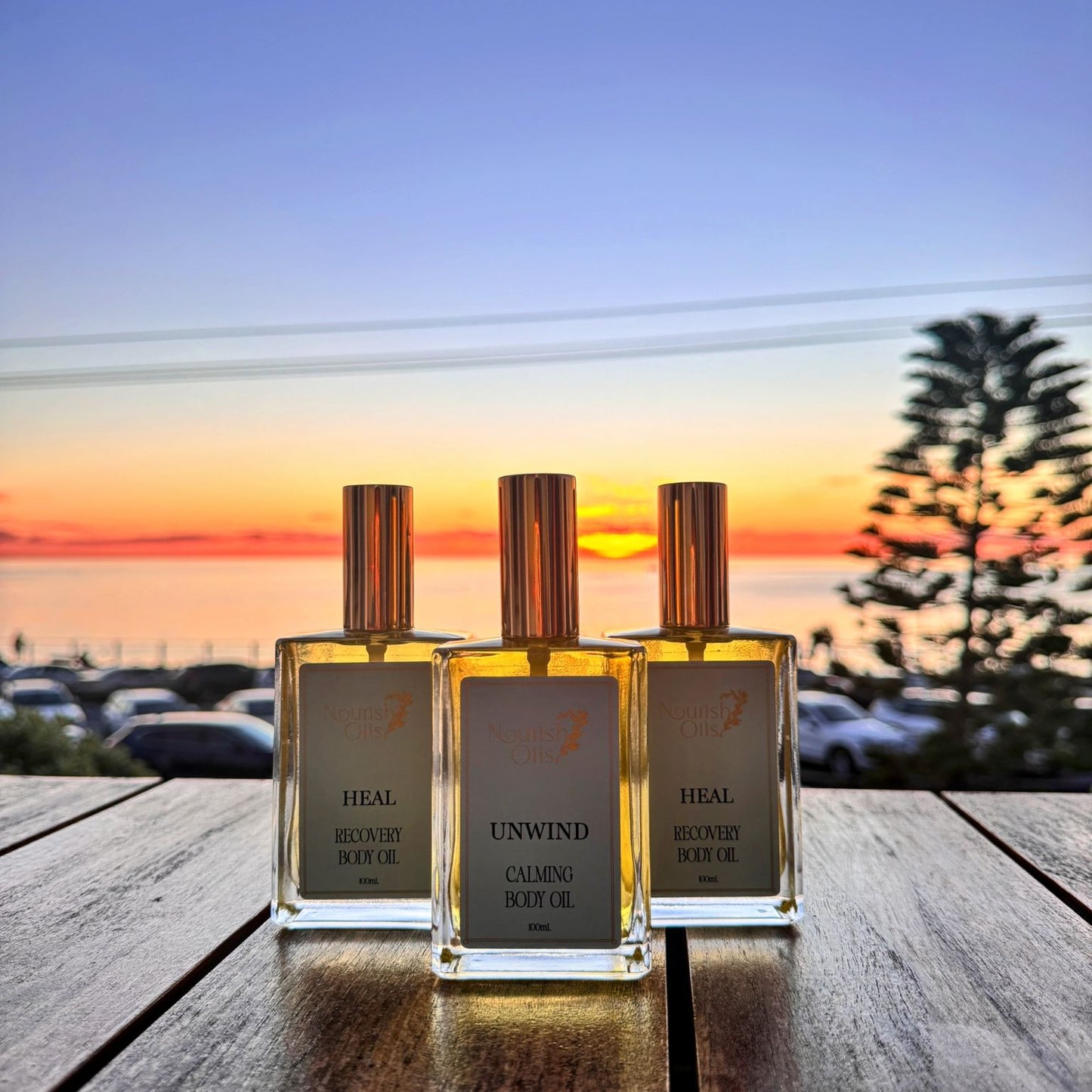 Three perfume bottles on a wooden surface with a sunset or sunrise in the background.