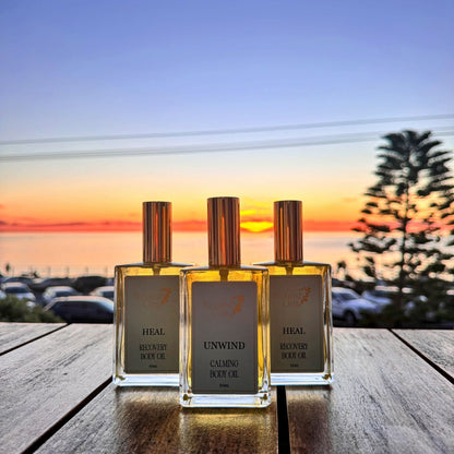 Three perfume bottles on a wooden surface with a sunset or sunrise in the background.