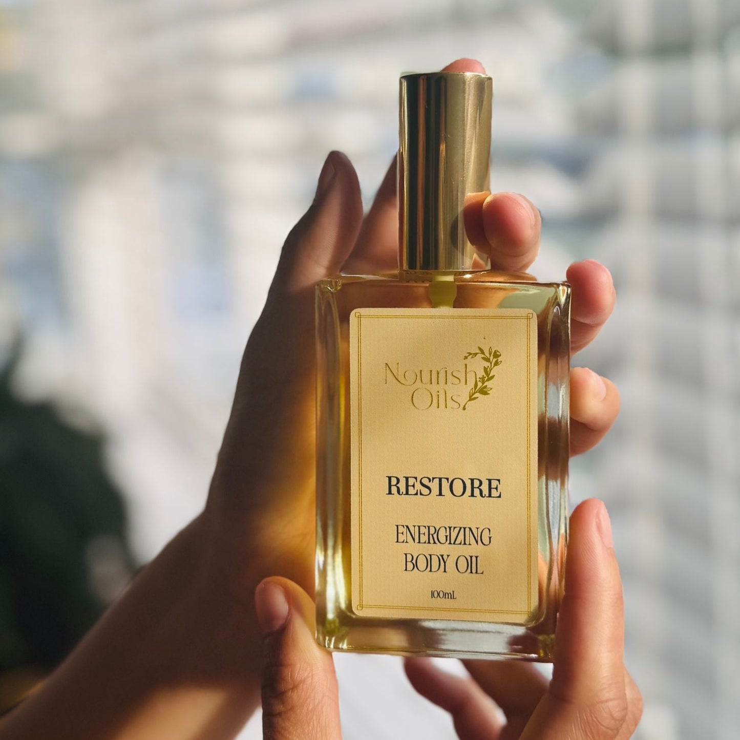 Hand holding a bottle of 'Restore' body oil with a blurred background