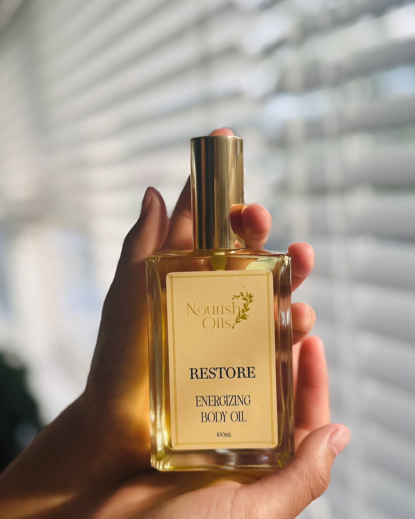 Hand holding a bottle of 'Restore' body oil with a blurred background